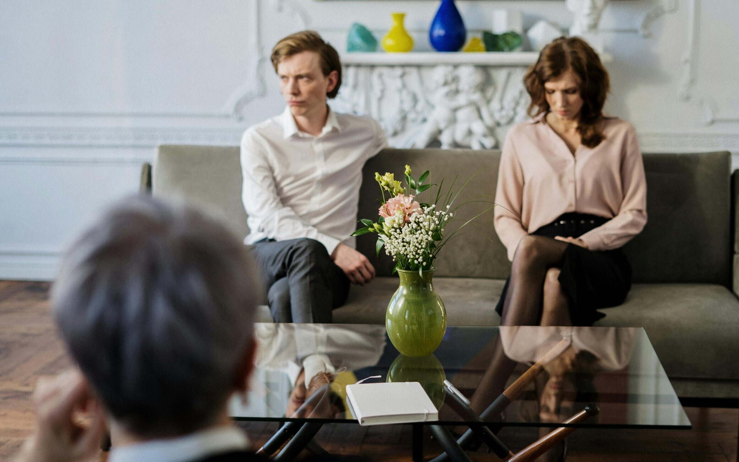 A couple sits on a sofa during a therapy session with a counselor, focusing on relationship issues.