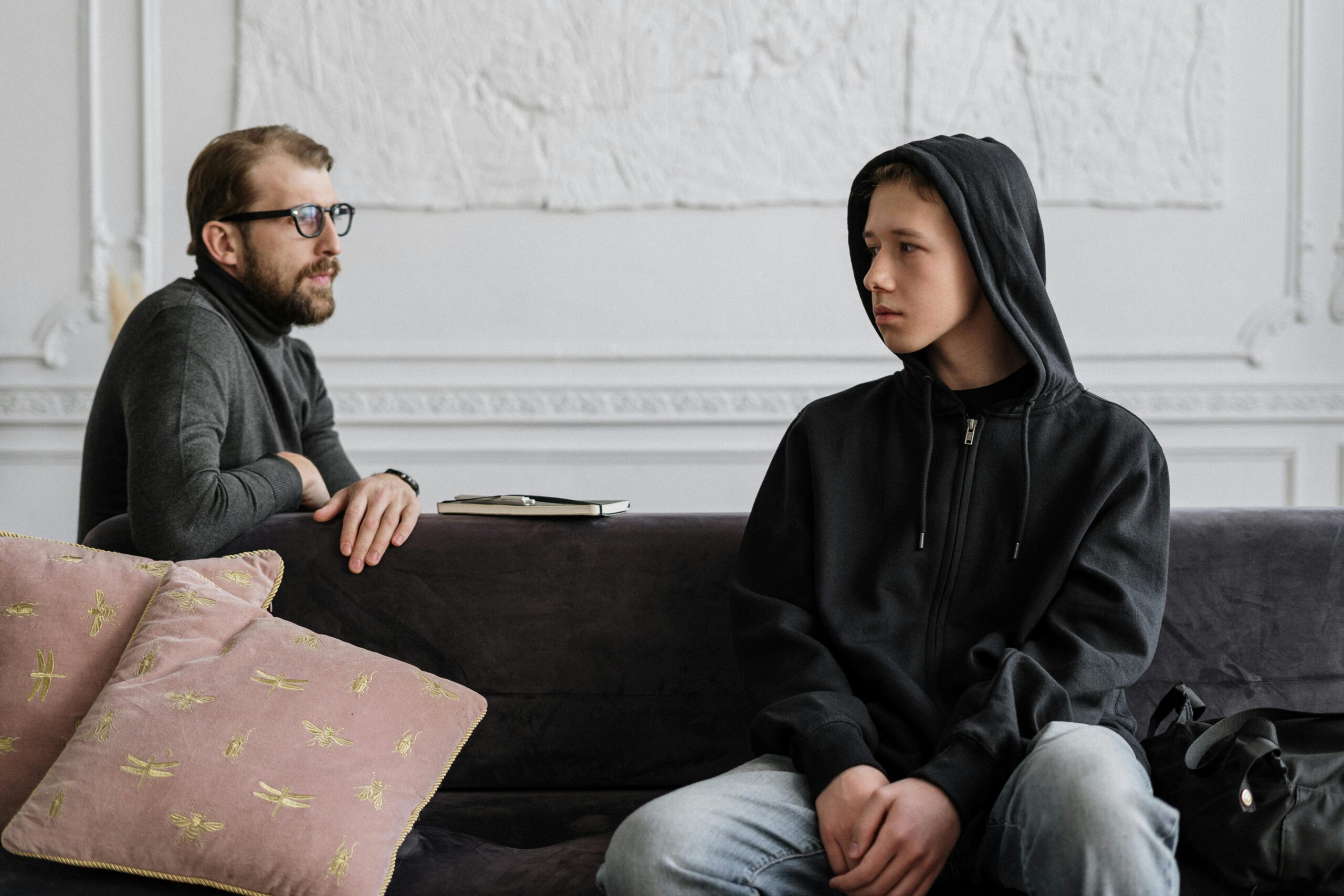 A therapist and a teenage boy discuss mental health issues in a modern office setting.