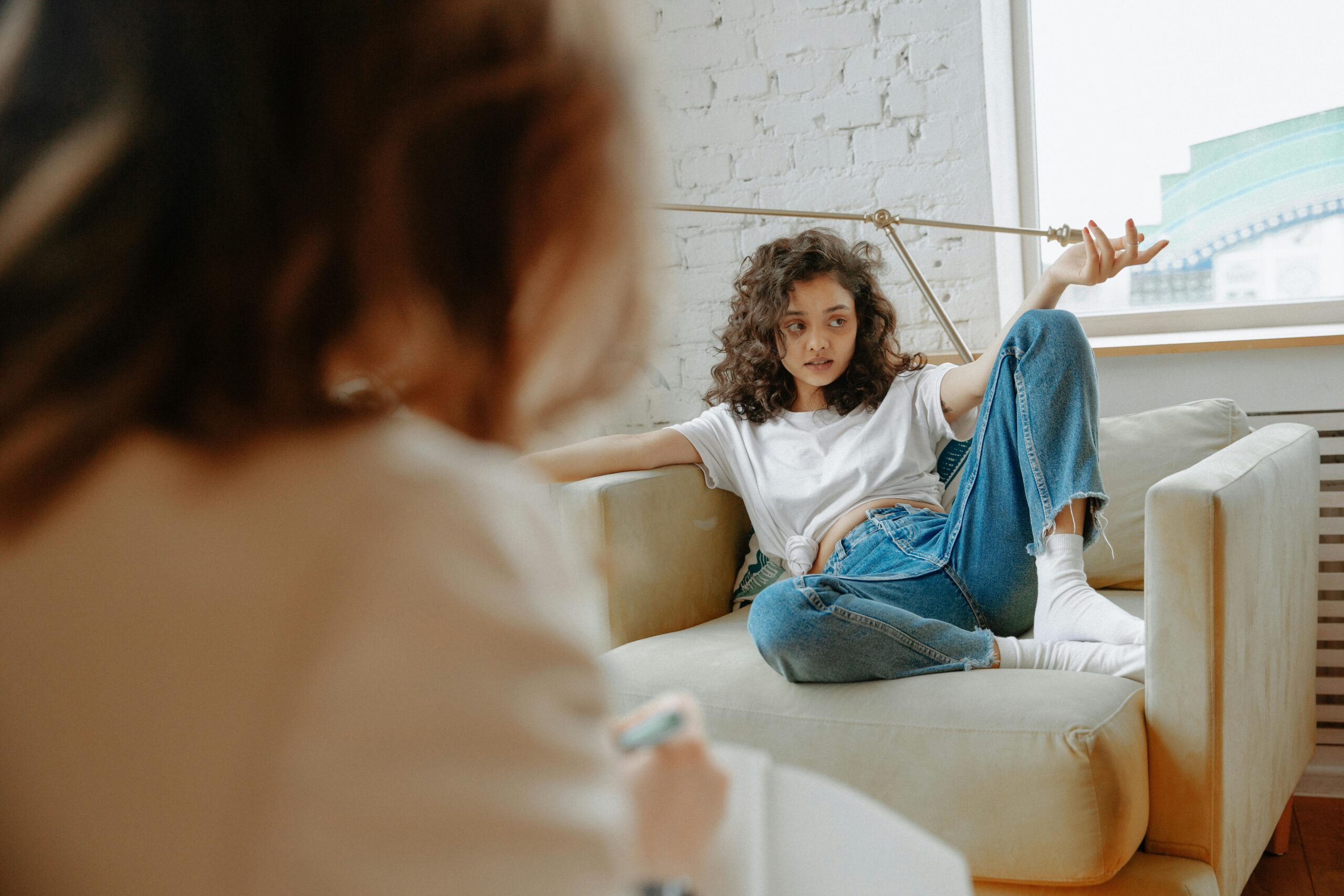 A teenager with curly hair receives counseling in a modern indoor setting, discussing mental health.
